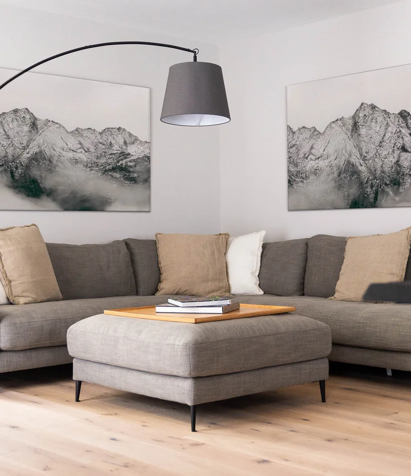Gemütliche Sitzecke mit grauem Ecksofa, Hocker, Stehlampe und Bergbildern