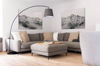 Gemütliche Sitzecke mit grauem Ecksofa, Hocker, Stehlampe und Bergbildern