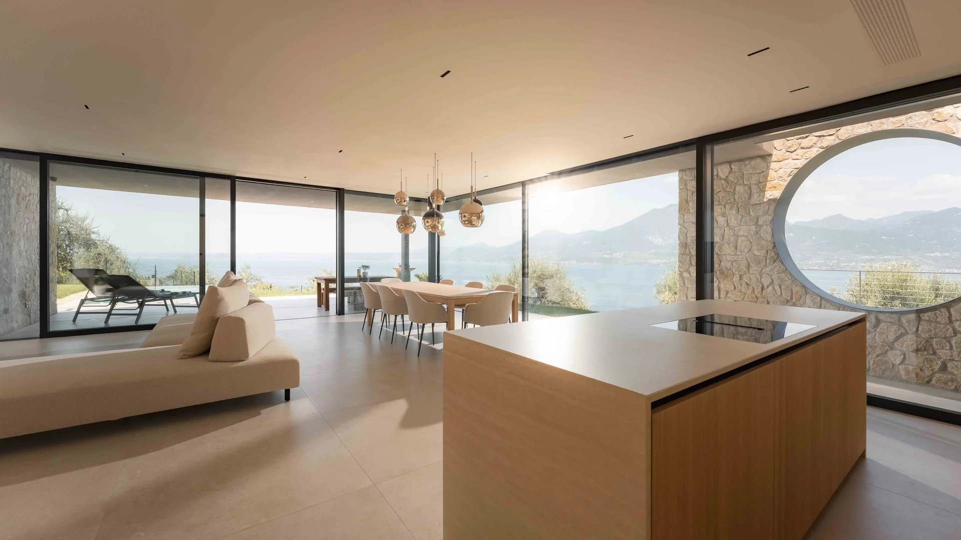 INTERIOS. Il tuo studio di interior design. Soggiorno moderno con cucina, tavolo da pranzo e vista panoramica sul lago e sulle montagne