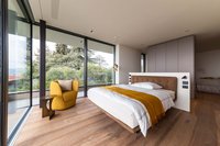 Modernes Schlafzimmer mit großen Fenstern und gelbem Sessel