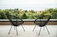 Zwei schwarze Stühle auf Balkon mit Blick auf grüne Bäume und Stadt im Hintergrund