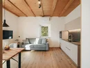 Soggiorno con soffitto in legno, divano grigio e cucina moderna