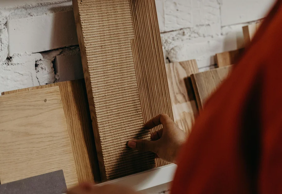 Persona sceglie campioni di legno da uno scaffale contro muro in mattoni bianchi