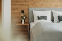 Modernes Schlafzimmer mit grauem Kopfteil und Holzwand mit Blumenvasen