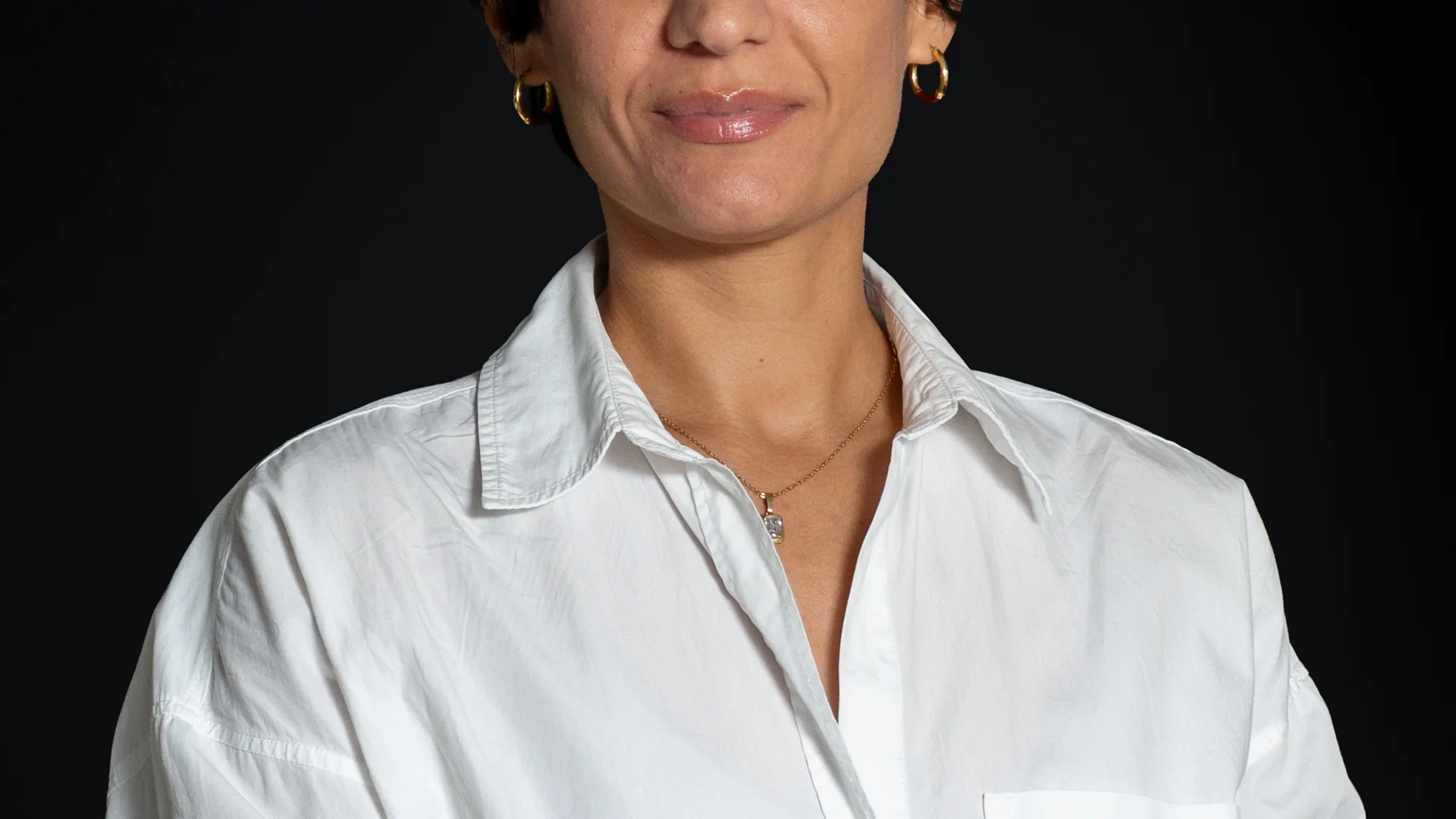 Ritratto di una donna con capelli corti e scuri e camicia bianca su sfondo scuro