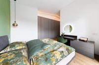 Modernes Schlafzimmer mit Blumenbettwäsche, Schreibtisch und runder beleuchteter Spiegel