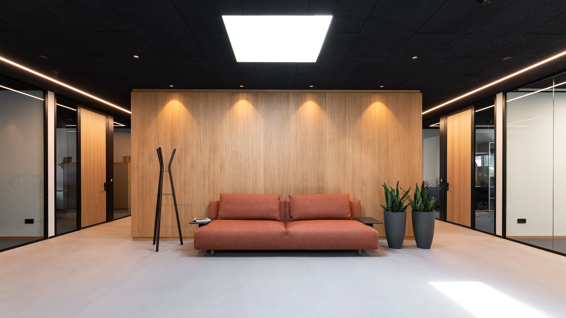 Moderne Empfangslounge mit rotem Sofa, Pflanzen und Holzverkleidung an der Wand