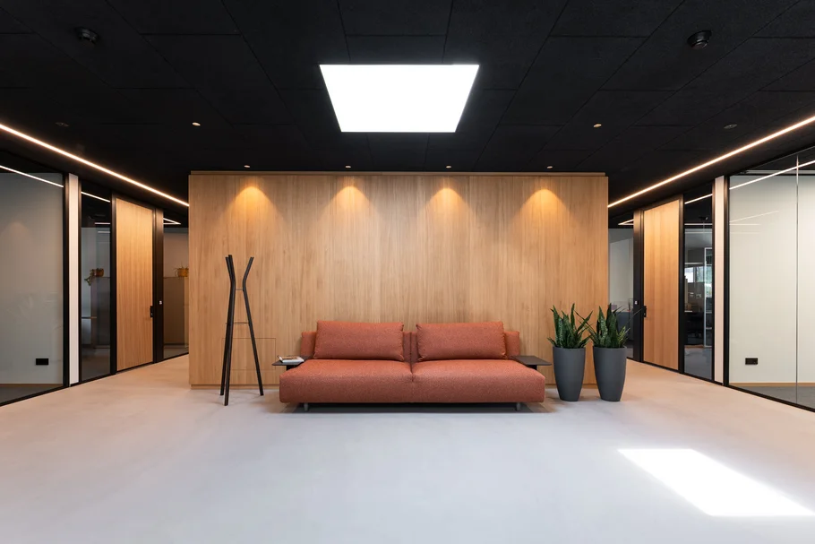 Moderne Empfangslounge mit rotem Sofa, Pflanzen und Holzverkleidung an der Wand