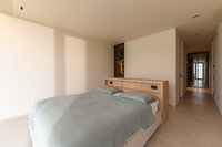 Helles Schlafzimmer mit Doppelbett, grauer Bettdecke und angrenzendem Flur