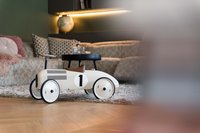 Weißes Kinderrennwagen-Spielzeug auf Holzboden vor einem Sofa