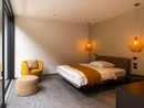 Modernes Schlafzimmer mit gelbem Sessel, Bett und warmen Hängelampen