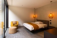 Modernes Schlafzimmer mit gelbem Sessel, Bett und warmen Hängelampen