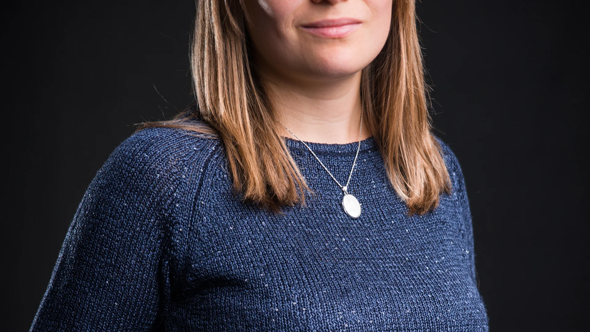 Frau mit Brille und blauem Pullover vor schwarzem Hintergrund