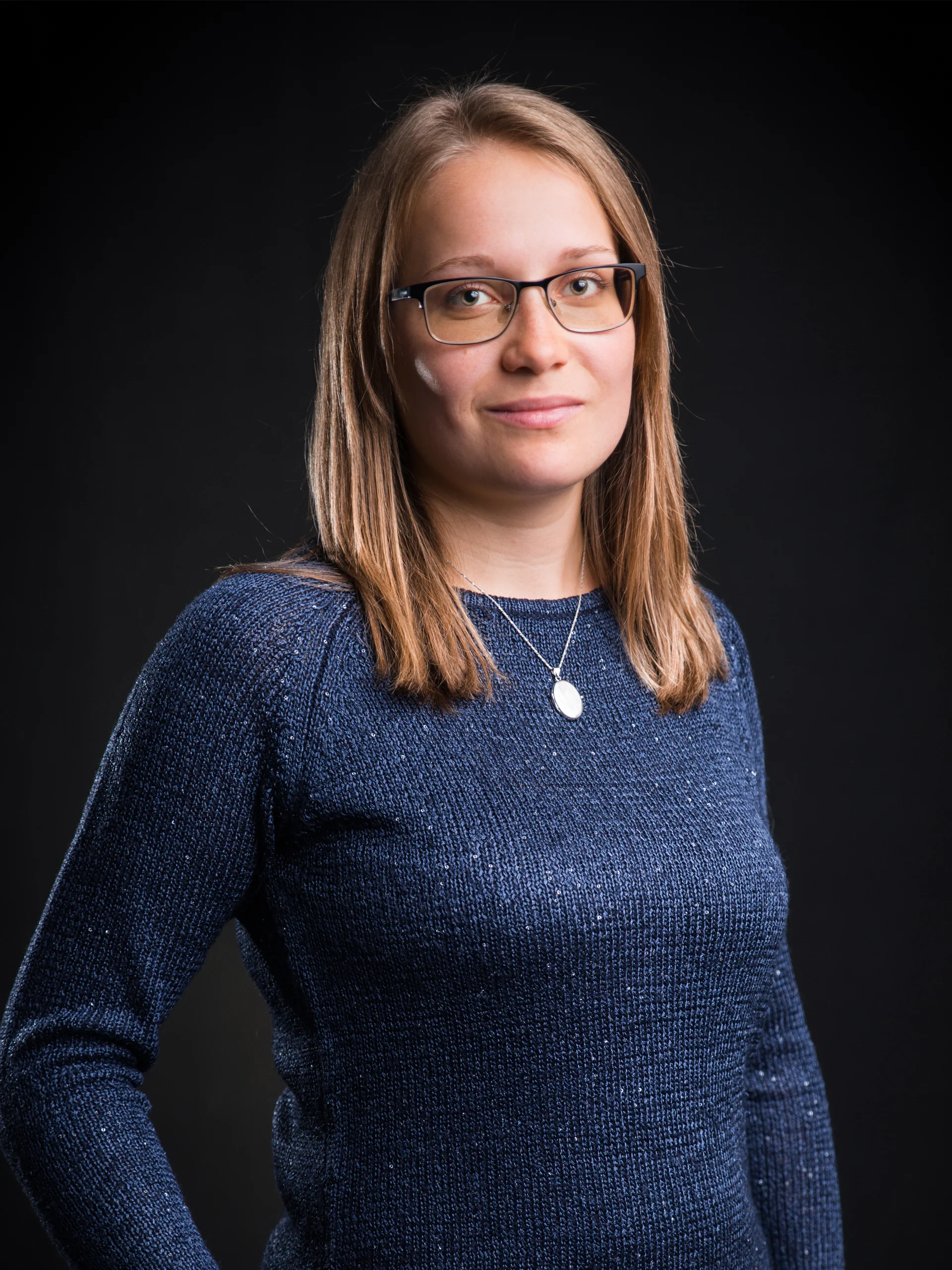 Frau mit Brille und blauem Pullover vor schwarzem Hintergrund