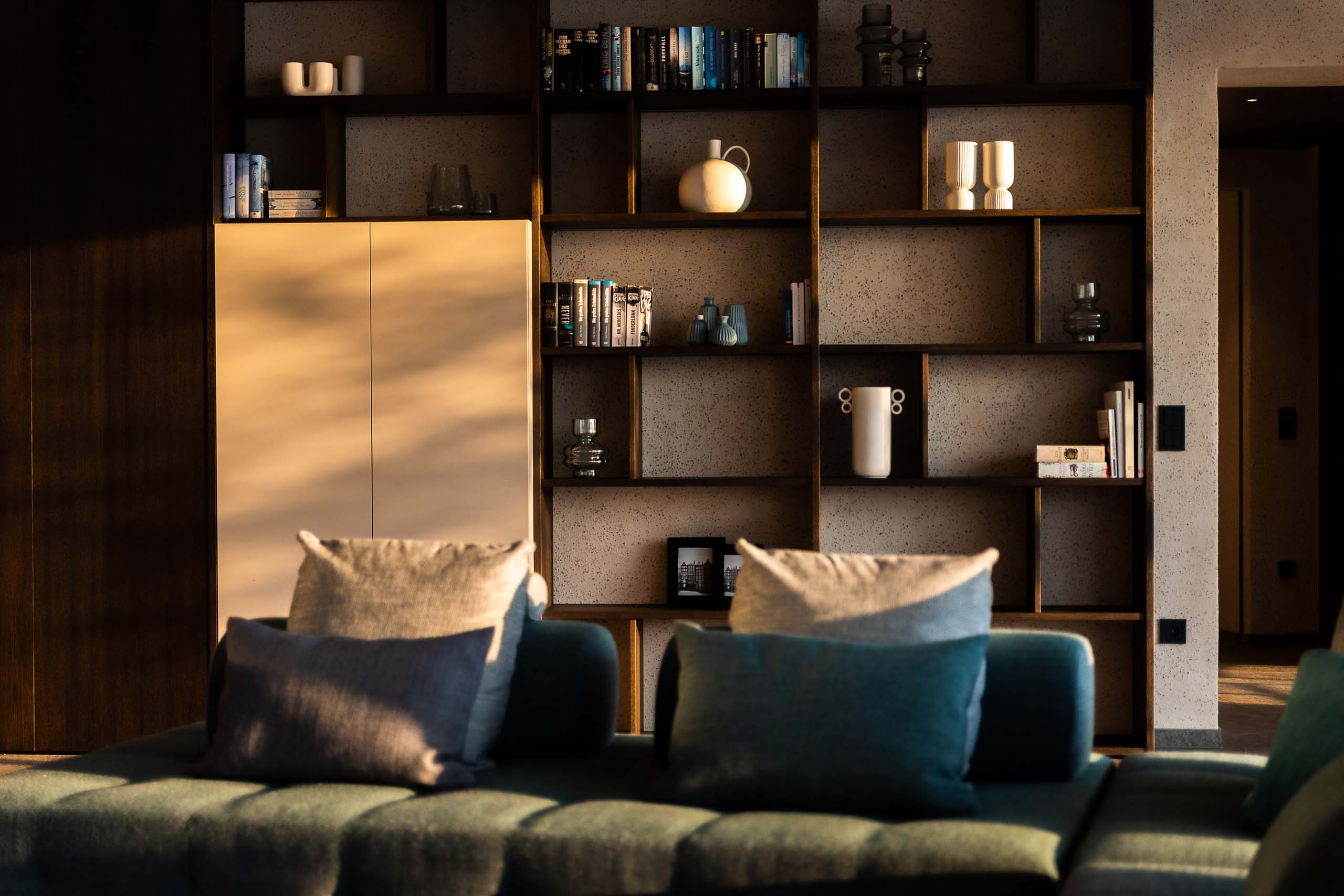 Modernes Wohnzimmer mit grünem Sofa und Bücherregal bei Sonnenlicht